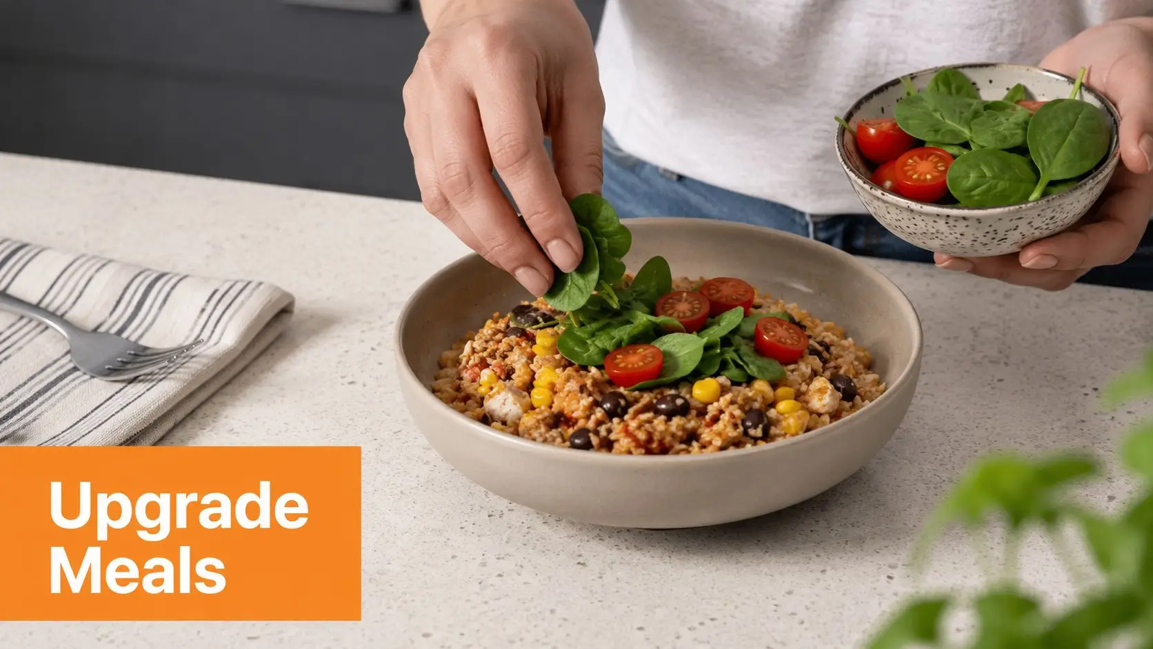 A person adding fresh spinach to a healthy bowl of grains, beans, corn, and cherry tomatoes.